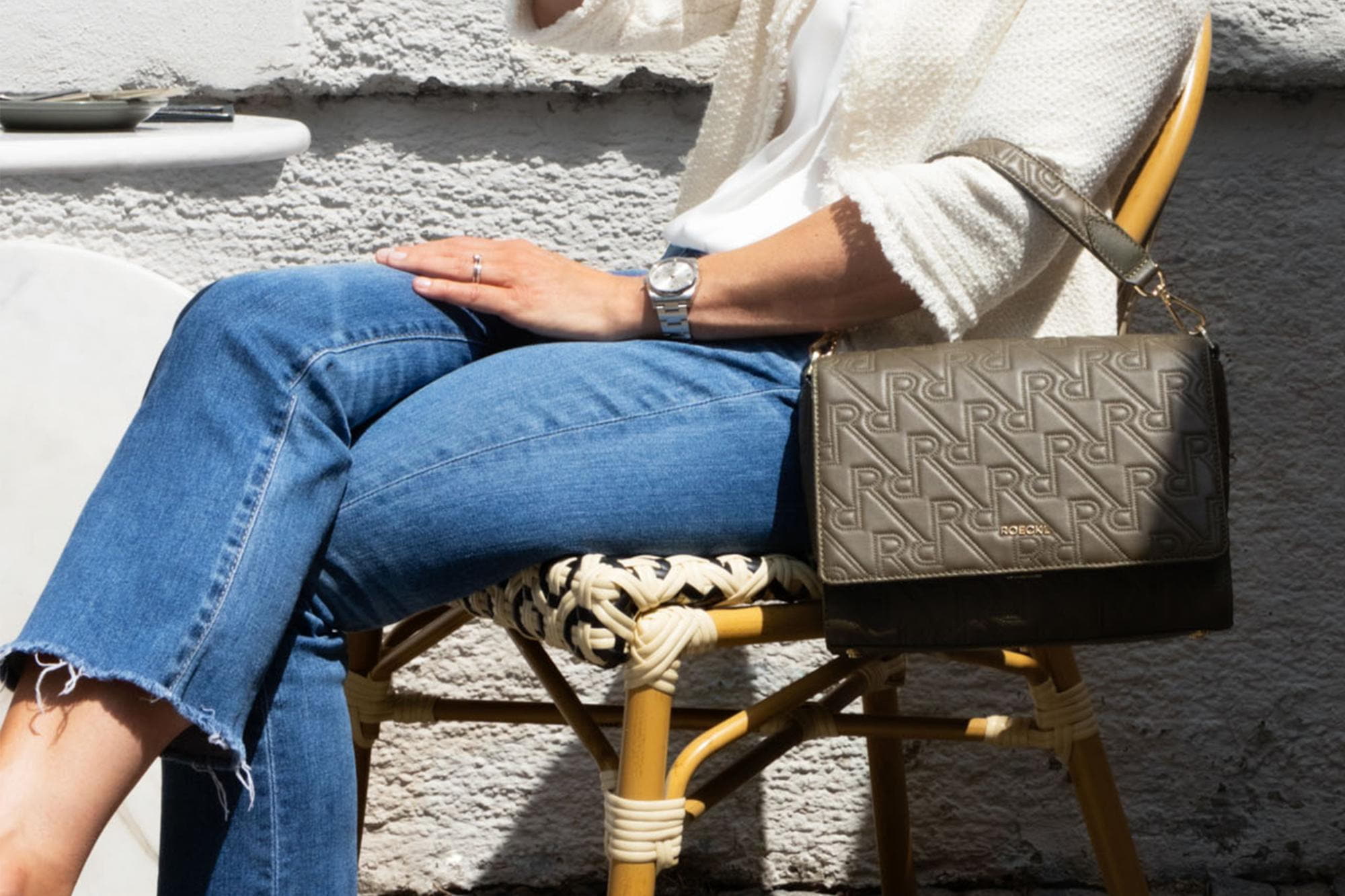 Frau mit geprägter ROECKL-Umhängetasche in Taupe – edle Crossbody-Bag mit charakteristischem RR-Monogramm und urbanem Chic.