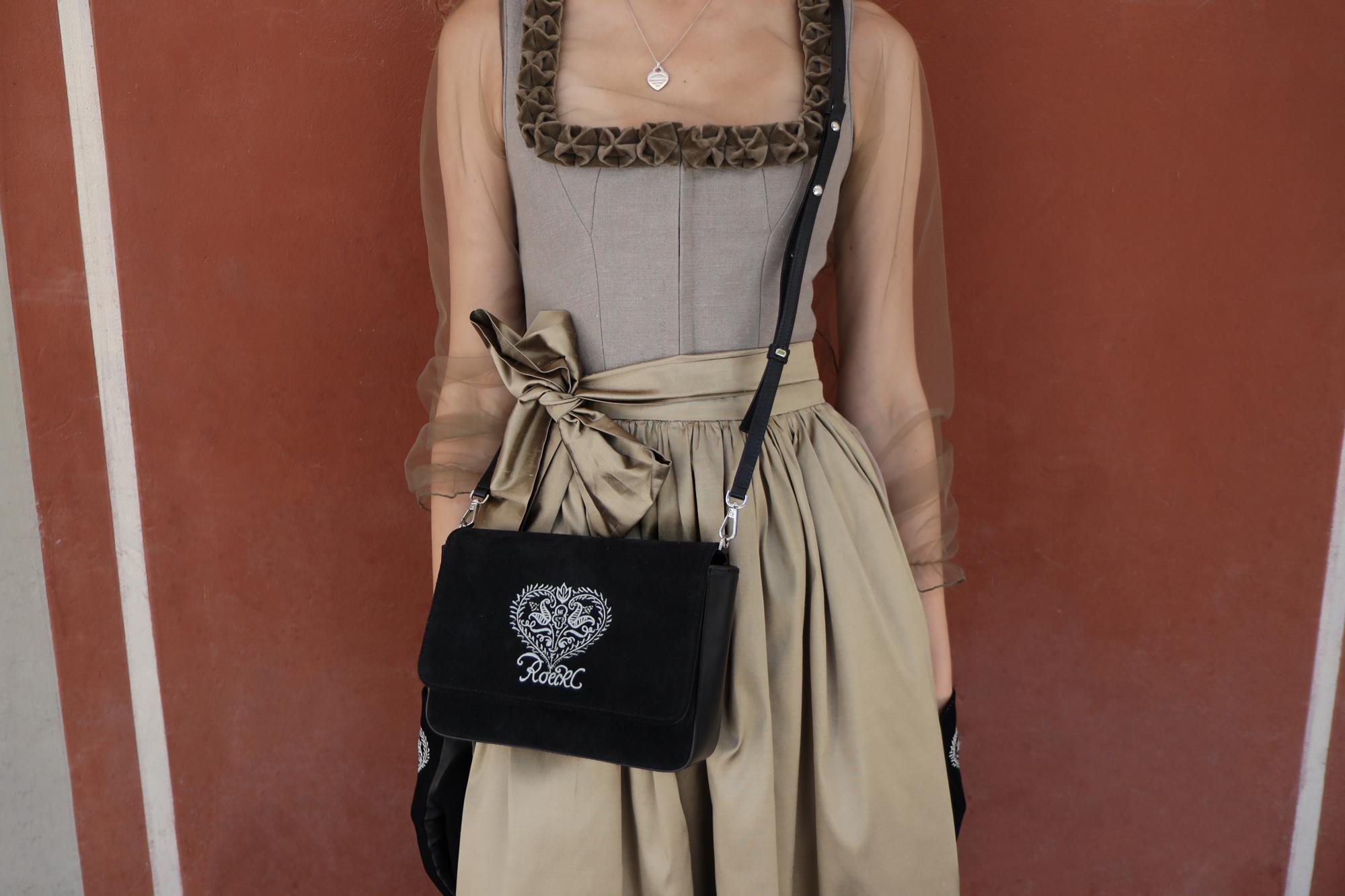 Frau im Dirndl trägt olivgrüne ROECKL-Handtasche und passende Wildlederhandschuhe mit Herzstickerei – perfektes Trachten-Ensemble für das Oktoberfest.
