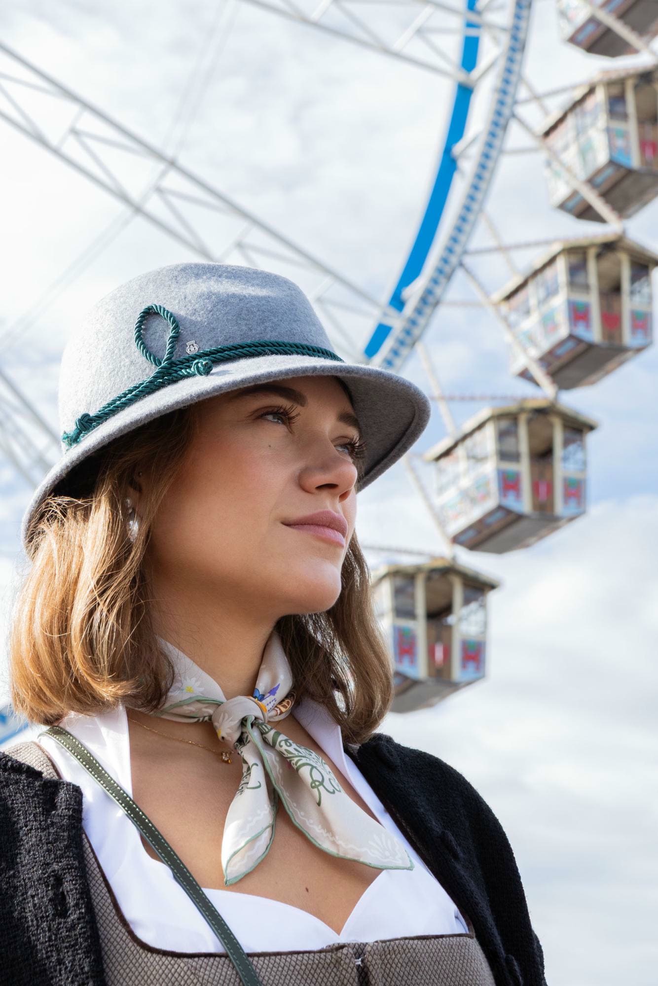 Frau trägt grauen ROECKL-Filzhut mit grüner Kordel und Seidentuch mit floraler Stickerei – klassischer Trachtenstil mit modernen Details.