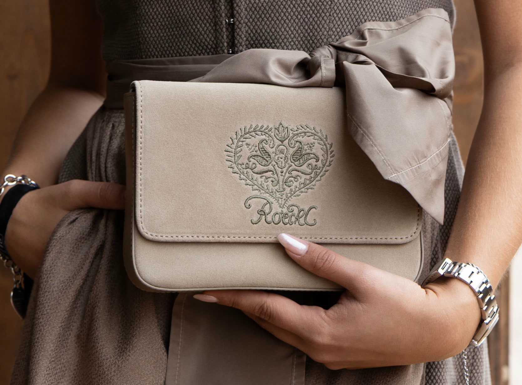 Detailaufnahme einer beigefarbenen ROECKL-Tasche aus Wildleder mit gesticktem Herzmotiv – elegantes Accessoire zur Tracht.