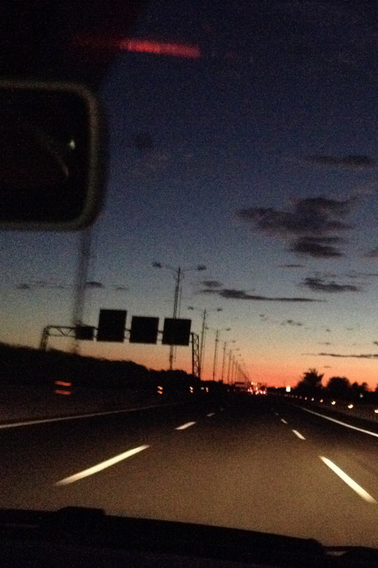 Blick aus dem Auto auf eine Landstraße bei Sonnenuntergang – stimmungsvolle ROECKL-Kampagnenszene, die Freiheit und Stil verbindet.