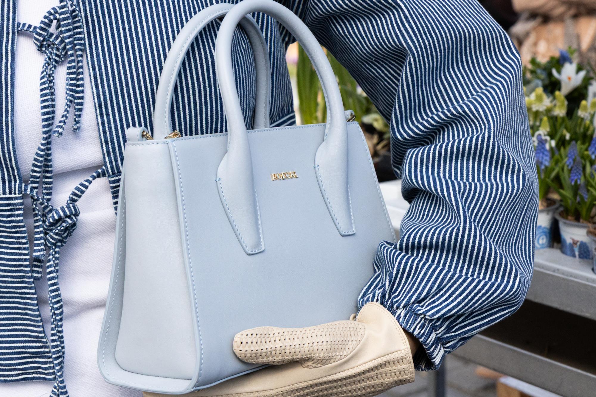 Nahaufnahme einer hellblauen Lederhandtasche und hellen Handschuuhen.