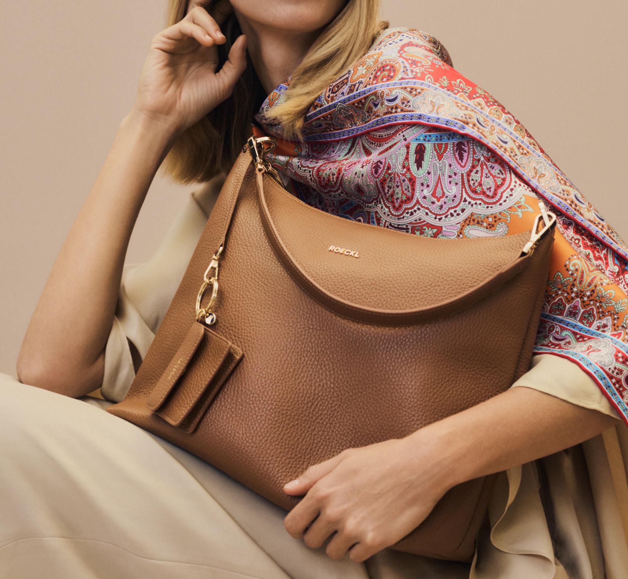 Eine stilvoll gekleidete Frau trägt das Mirror Paisley Seidentuch in orange und die Lederhandtasche Diana in braun.