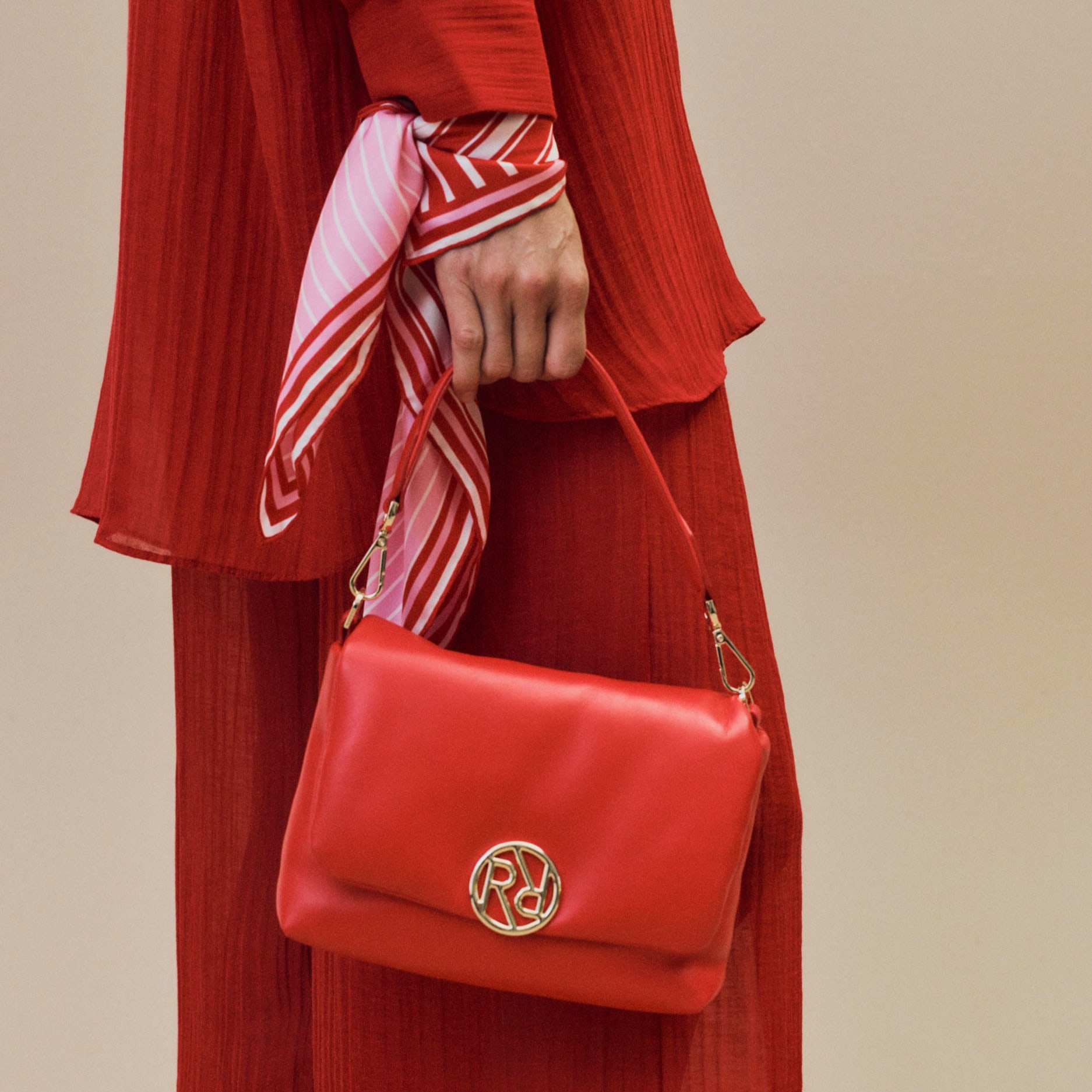 Eine stilvoll rot gekleidete Frau trägt die Soho Ledertasche in rot und ein farblich passendes Nickituch aus Seide in rot und rosa.