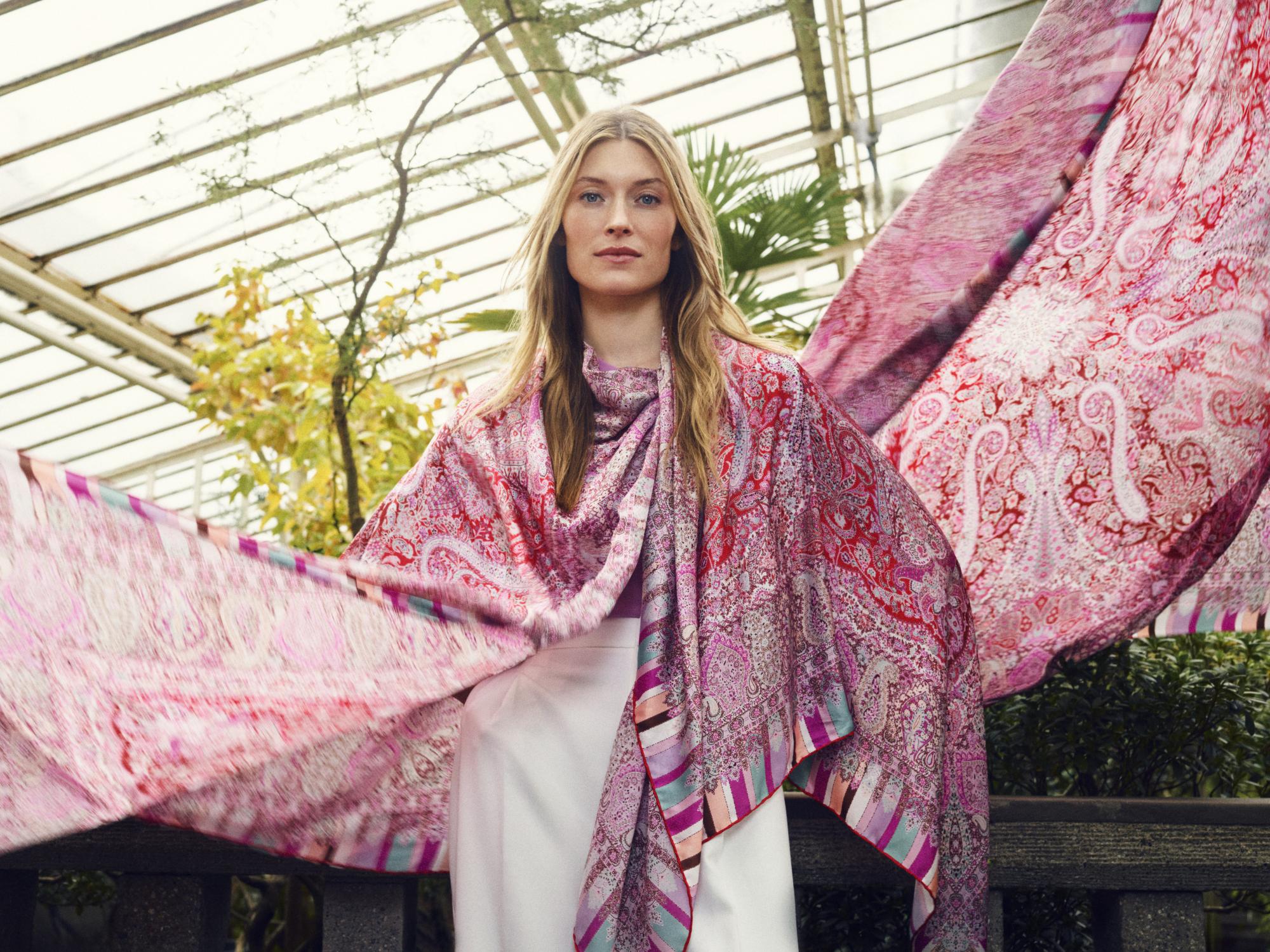 Eine stilvoll gekleidete Dame die zwei bunte Seidentücher mit Blumenprint schwingt.