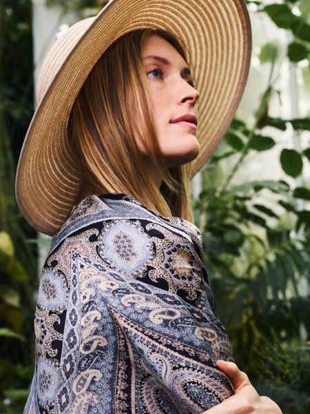 Frau mit Strohhut und gemustertem Seidenschal in botanischer Gartenkulisse