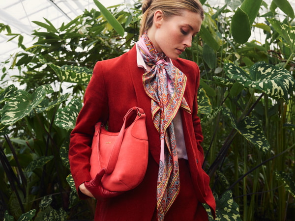 Woman wearing a red ROECKL silk scarf and carrying a red ROECKL leather handbag.