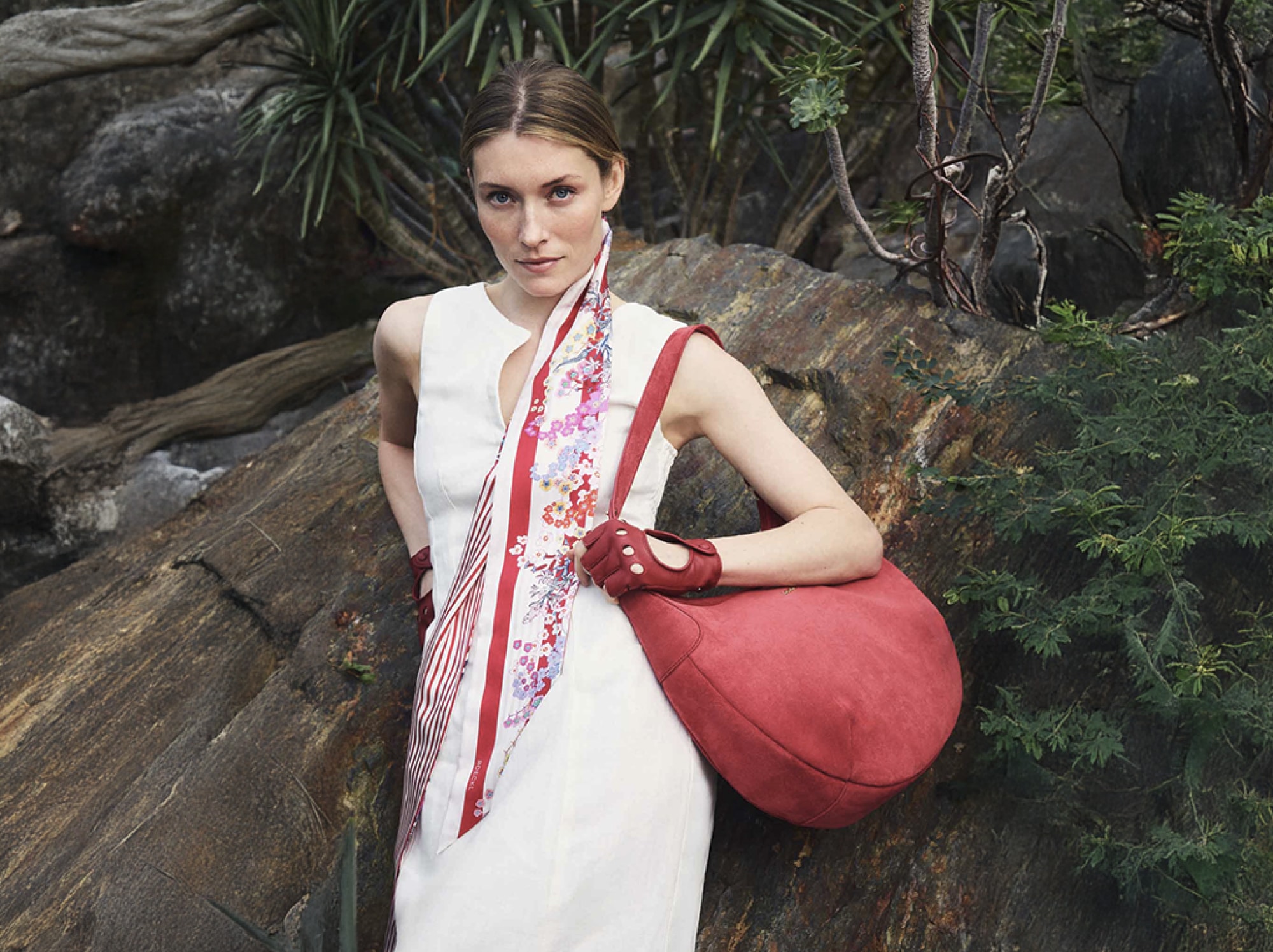Frau im roten Anzug mit gemustertem Seidenschal und roter Handtasche von ROECKL im botanischen Garten