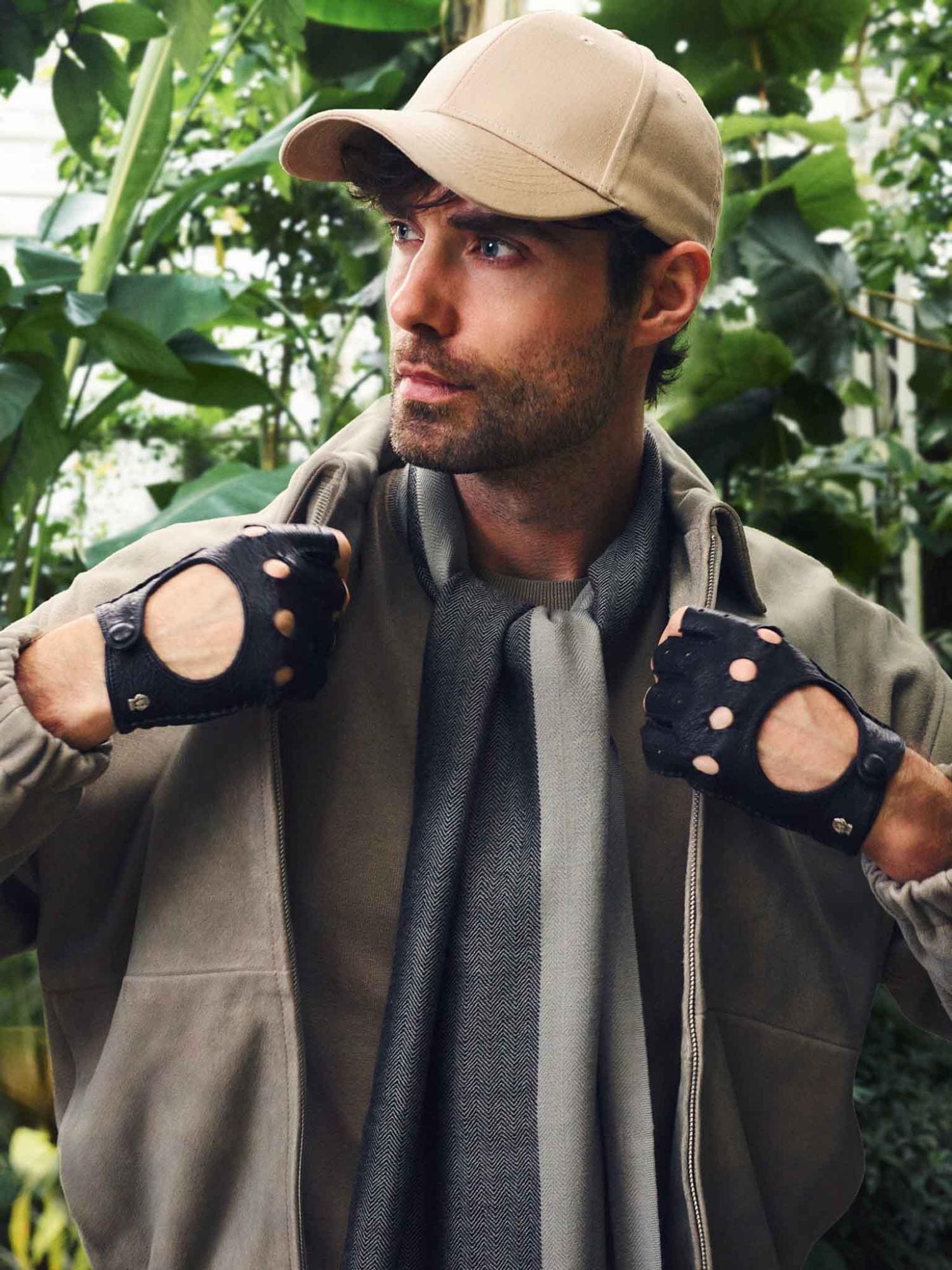 Mann mit schwarzem Schal und schwarzen Lederhandschuhen von ROECKL in heller Jacke in einer grünen Gartenlandschaft