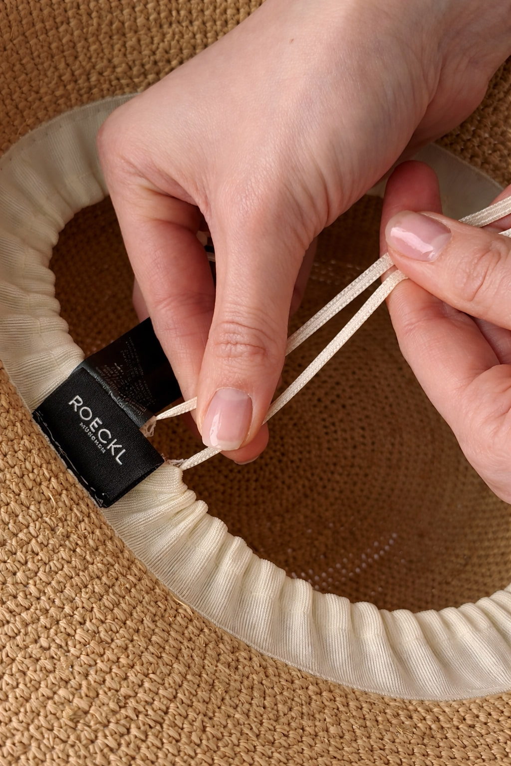 Frau mit beigem ROECKL-Bucket Hat und goldenen Ohrringen – moderner Sommerhut aus hochwertigem Material für einen trendigen Look.