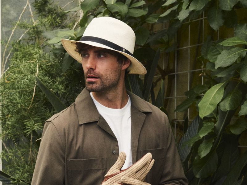 Roeckl helle Handschuhe werden von einem Mann mit Strohhut vor dichter Pflanzenkulisse in den Händen gehalten.