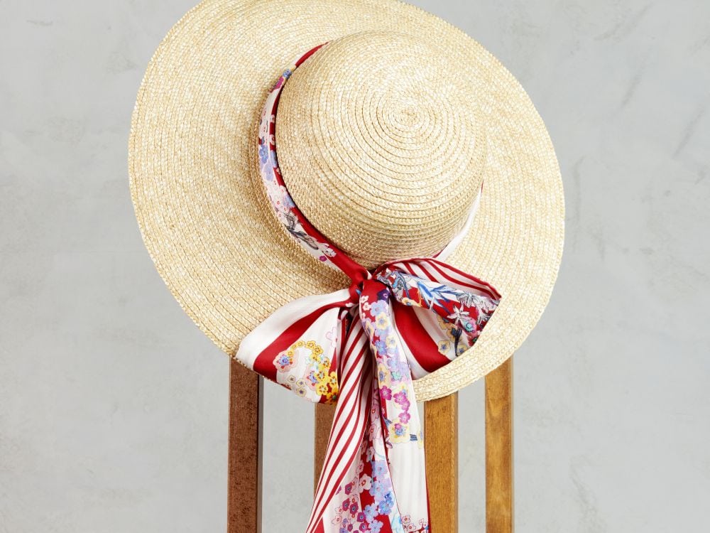 Roeckl Seidenschal mit floralem Muster ist stilvoll um einen Strohhut gebunden und wird vor hellem Hintergrund präsentiert.
