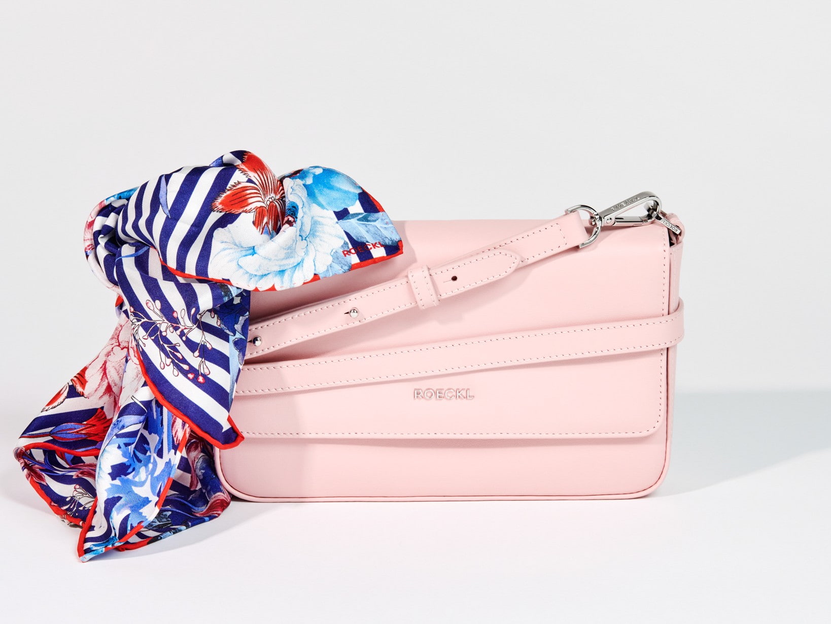 Roeckl Seidenschal mit floralen und grafischen Mustern liegt elegant auf einer rosafarbenen Lederhandtasche im Studio-Setting.