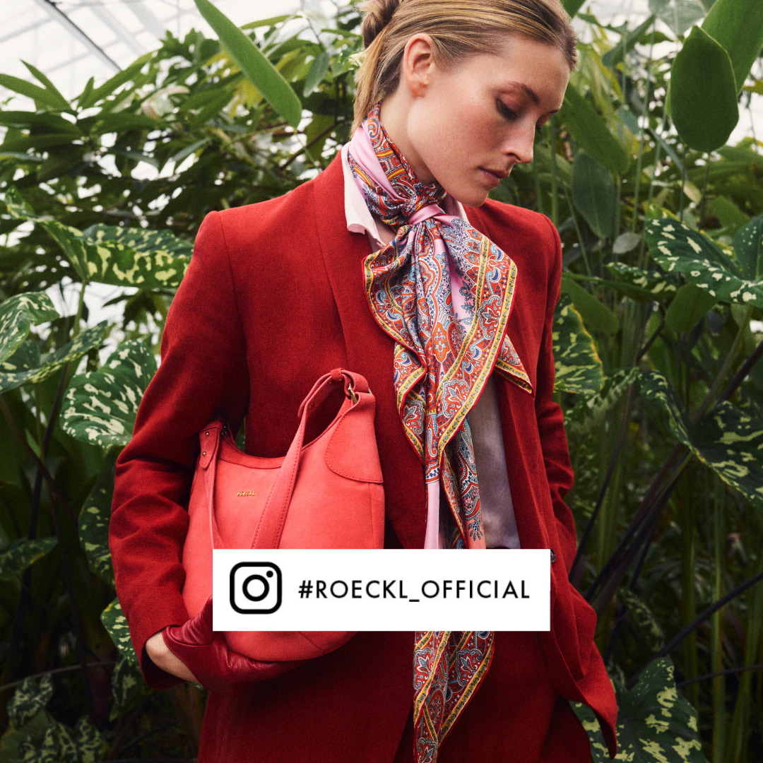 Eine Dame trägt rote Handschuhe, eine kleine passende Tasche und ein buntes Tuch über den Schulter.