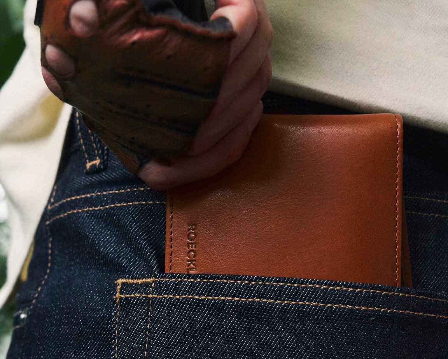 Drei ROECKL-Ledergeldbörsen in Cognacbraun und Dunkelblau auf rotem Hintergrund – elegante, hochwertige Accessoires aus feinem Leder.