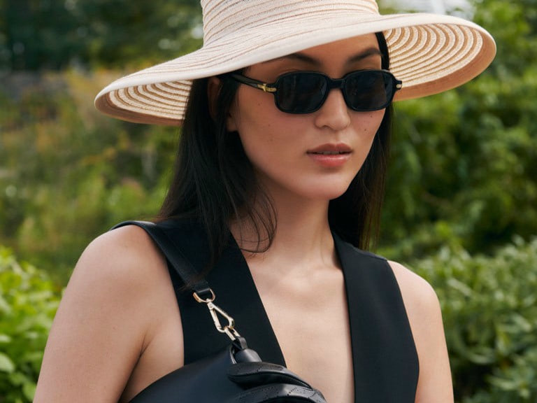 Frau mit schwarzer ROECKL-Lederhandtasche, breitem Strohhut und Sonnenbrille – elegantes Sommeraccessoire für einen stilvollen, modernen Look.