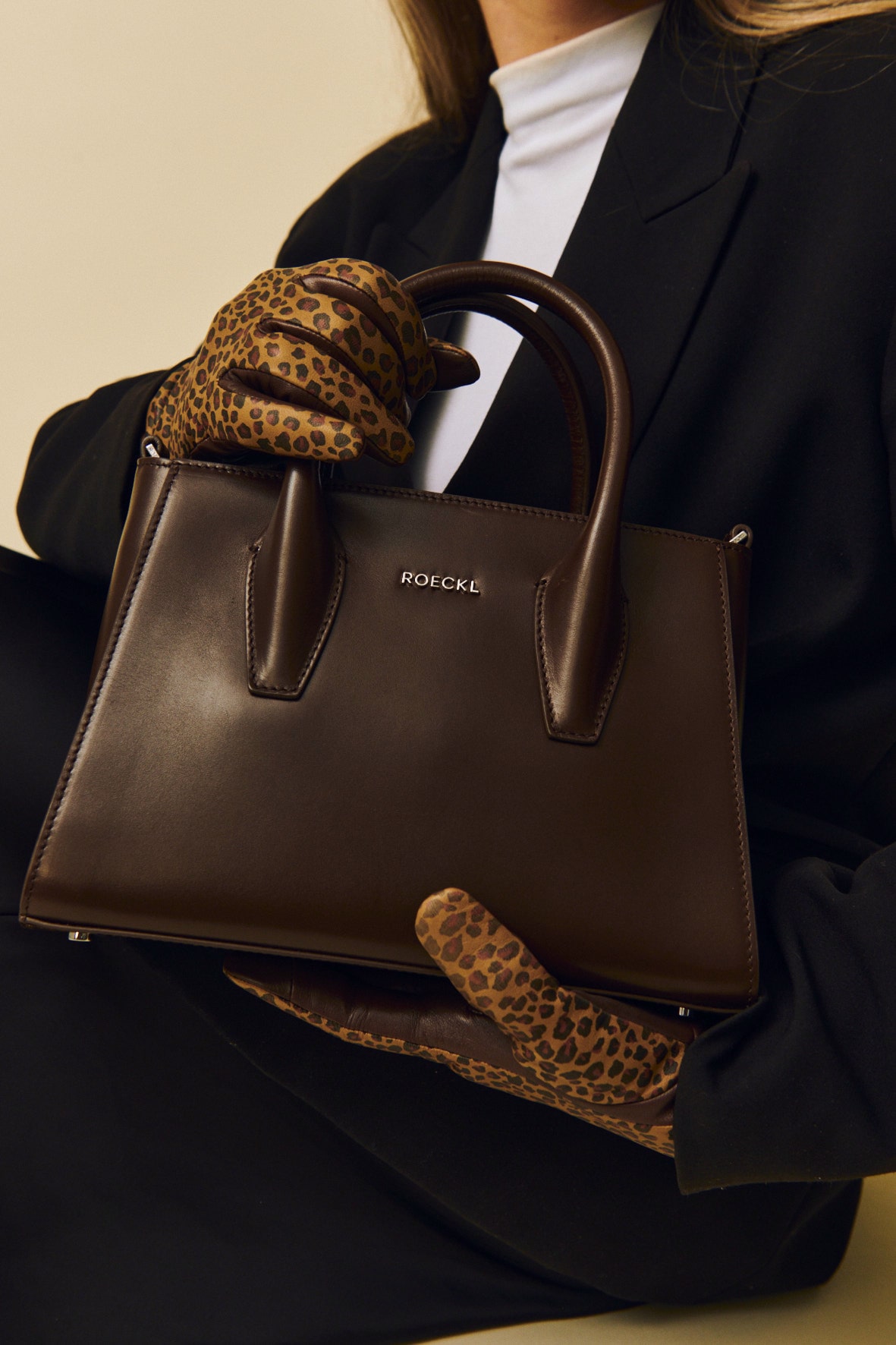 Eine blonde Dame trägt ein blau rot gemustertes Tuch um den Hals gebunden und hält eine strukturierte Ledertasche in rosa.