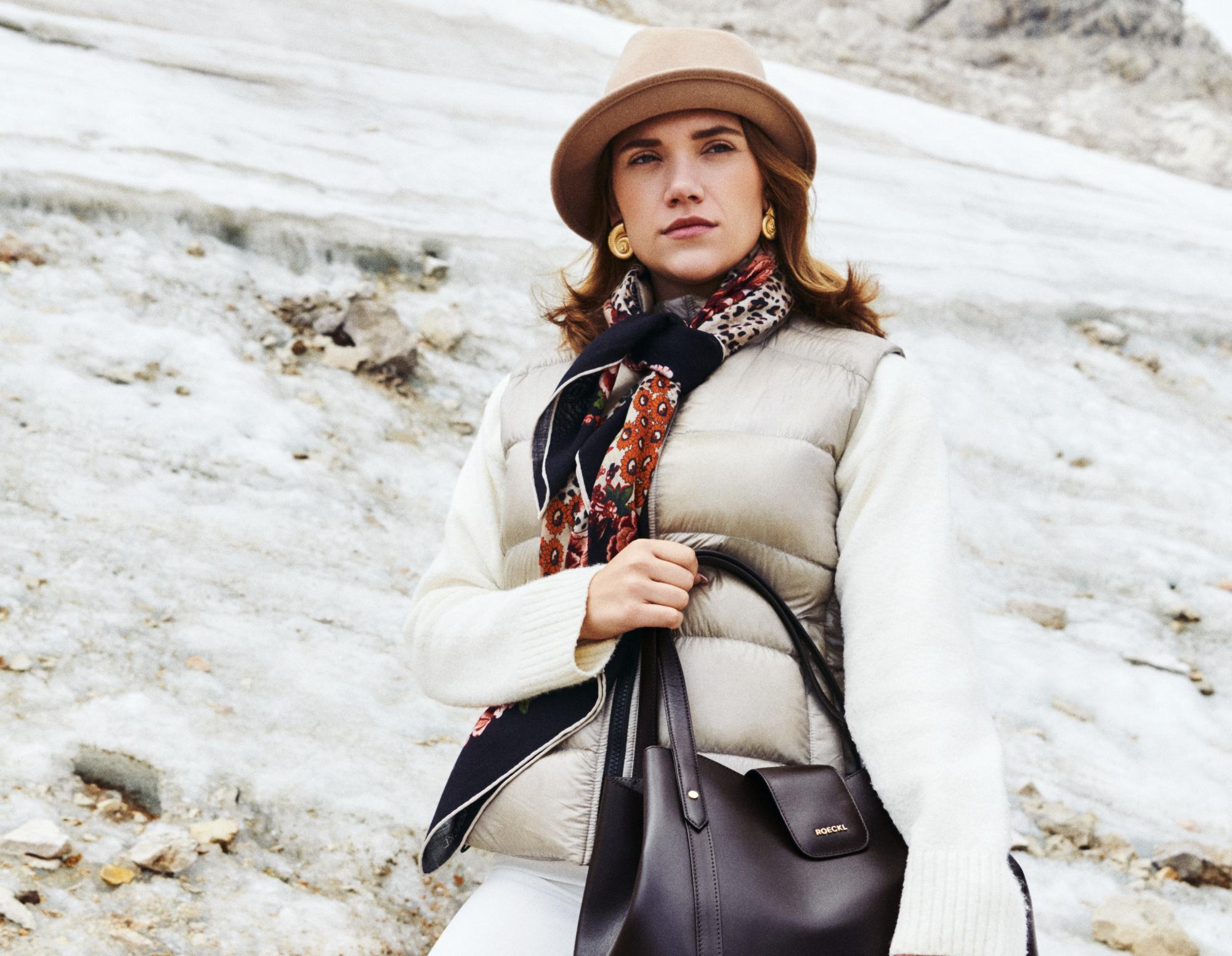 Eine blonde Frau mit schulterlangem Haar trägt ein großes, buntes Seidentuch mit roten Mohnblumen, blauen Streifen und floralen Skizzen.