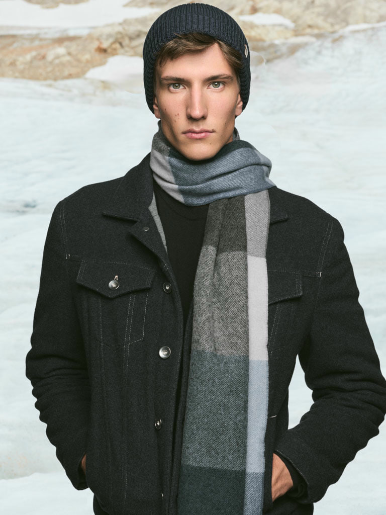 Ein elegant gekleideter Herr mit einem leichten Tuch in grau um den Hals und einer Leinenkappe.