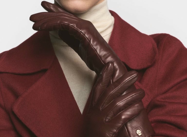 Eine junge blonde Dame trägt hochwertige Kurzfinger-Autofahrerhandschuhe aus hellem Peccary Leder.