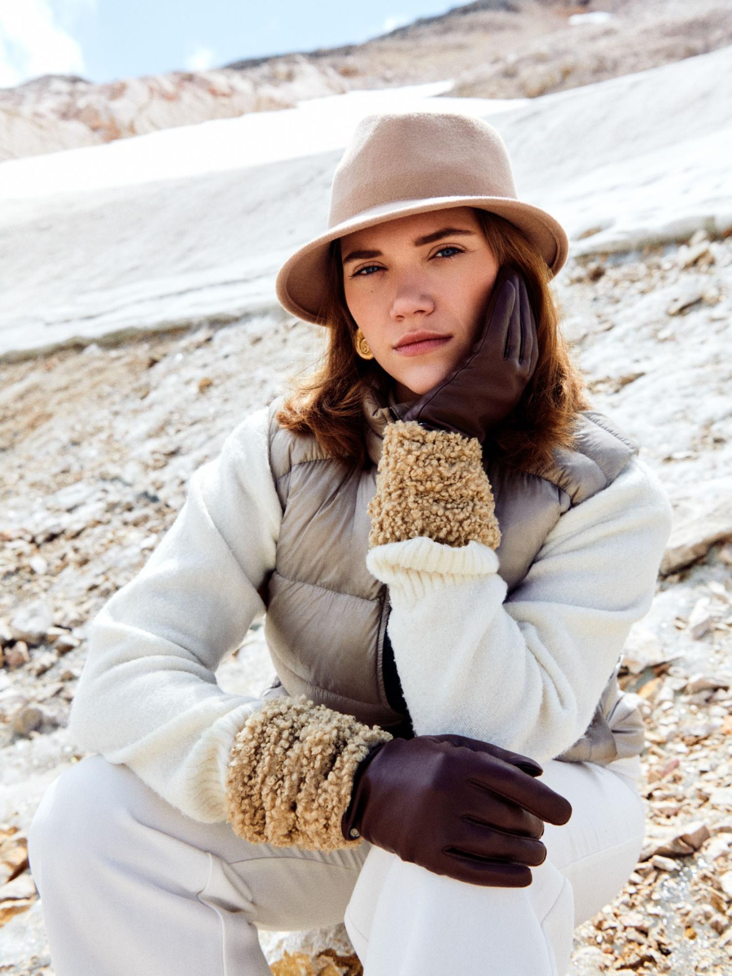 Blonde Dame trägt ein großes Seidentuch um die Schultern und hält eine braune Ledertasche in der Hand.