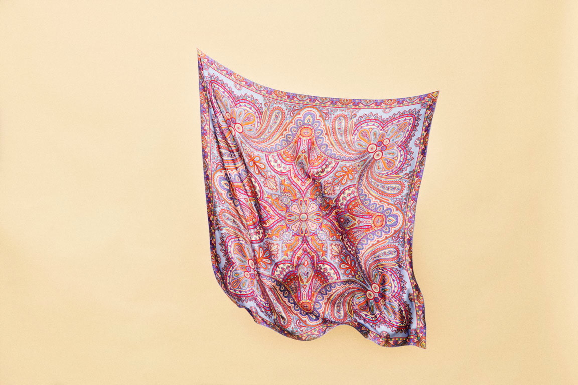 Eine Frau in einem schwarzen Blazer hat ein gemustertes Tuch über ihre Schulter drapiert.