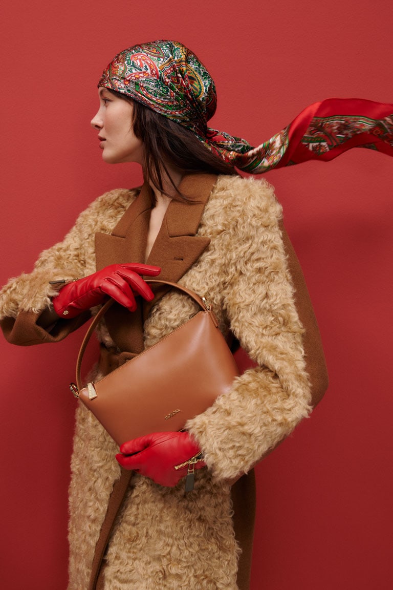 Frau mit braunem Mantel, roter ROECKL-Ledertasche und roten Lederhandschuhen – luxuriöse Accessoire-Kombination mit farbenfrohem Seidentuch.