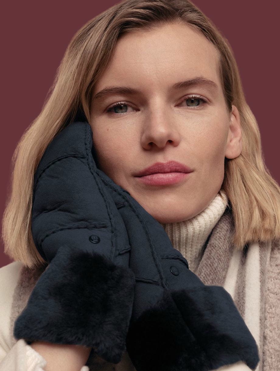 Blonde Dame trägt ein großes Seidentuch um die Schultern und hält eine braune Ledertasche in der Hand.