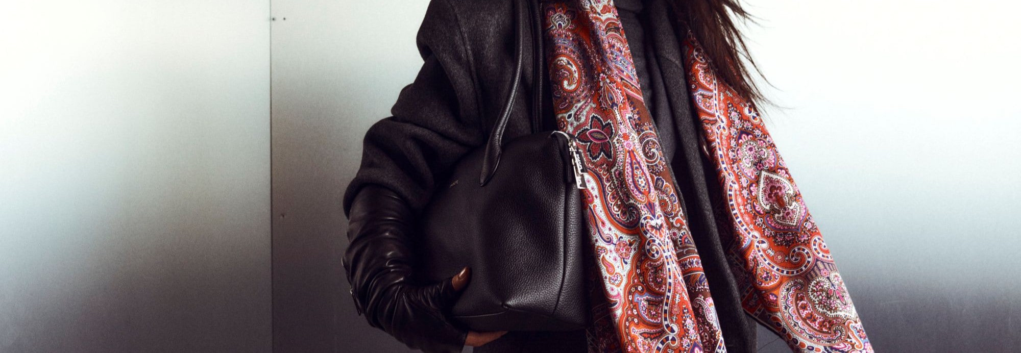 Roeckl Lederhandtasche in Schwarz wird von einer eleganten Frau im weißen Blazer in einer urbanen Straßenszene mit historischer Architektur getragen.