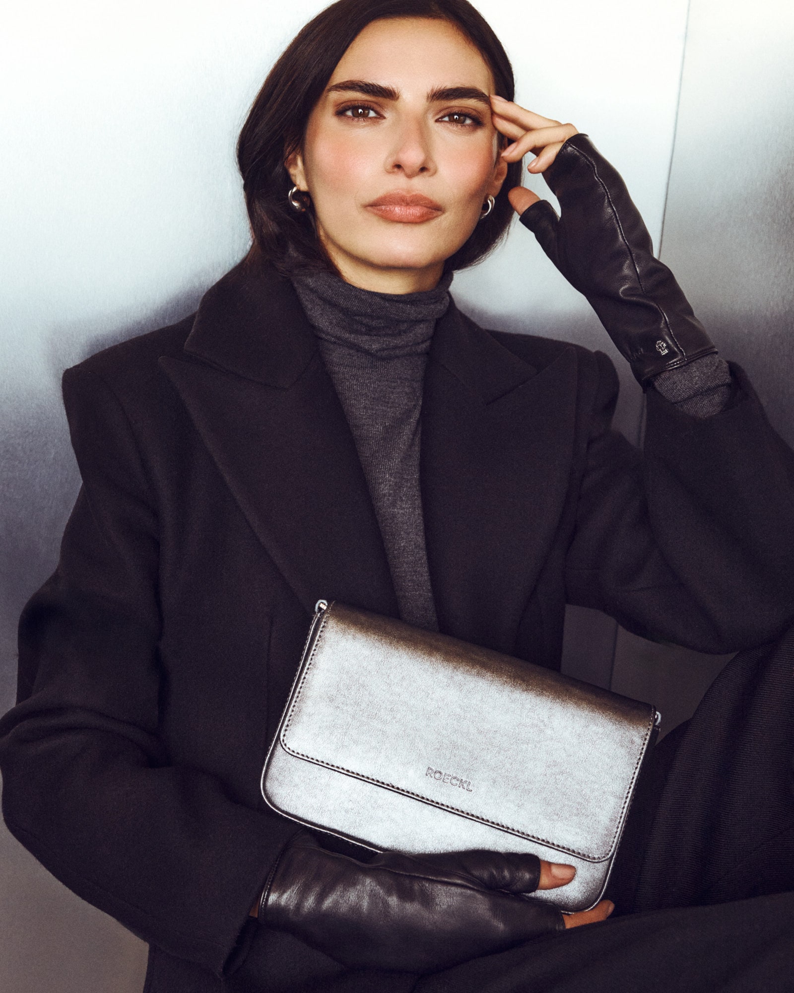 Roeckl lange schwarze Lederhandschuhe werden von einer Frau zu einem eleganten Abendkleid kombiniert, während sie eine silberne Clutch hält.
