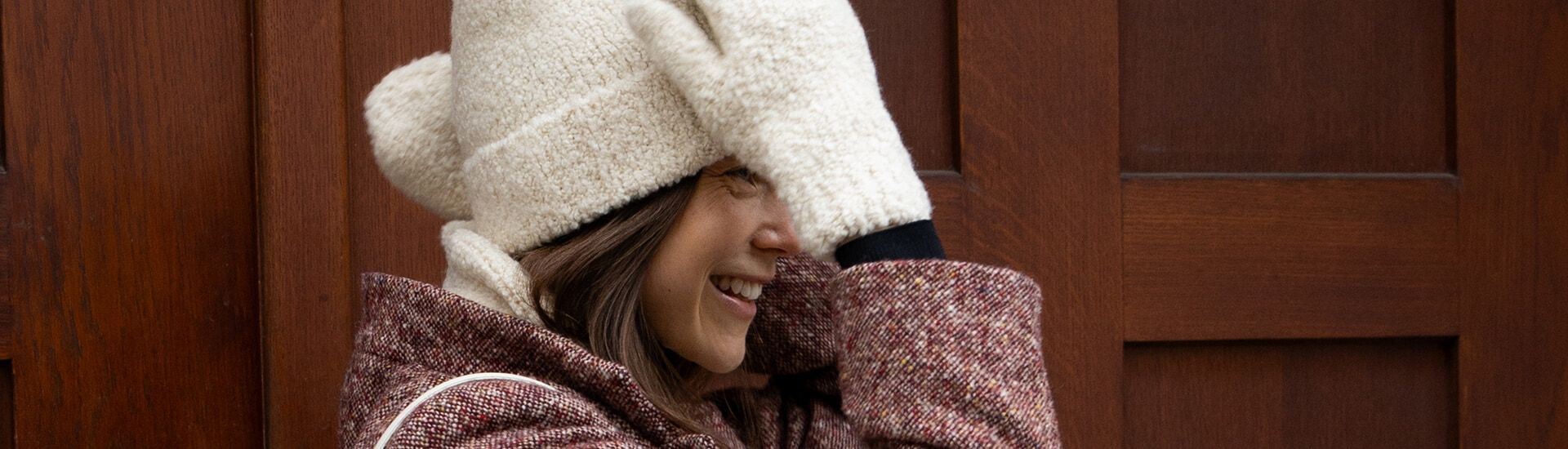 Lachende Frau mit ROECKL Strick-Handschuhen/Fäustlingen, Strick-Schal und Strick-Mütze Warm Embrace woolwhite