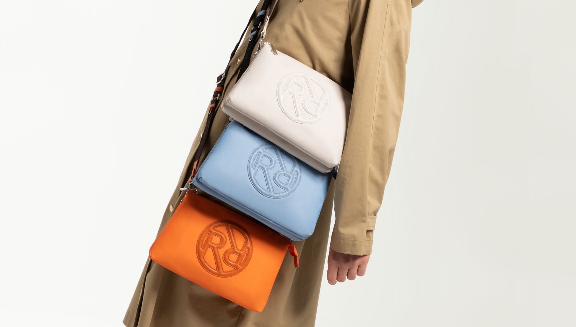 Frau mit beigem Trenchcoat trägt drei kleine ROECKL Nylon Taschen in orange, blau und beige.