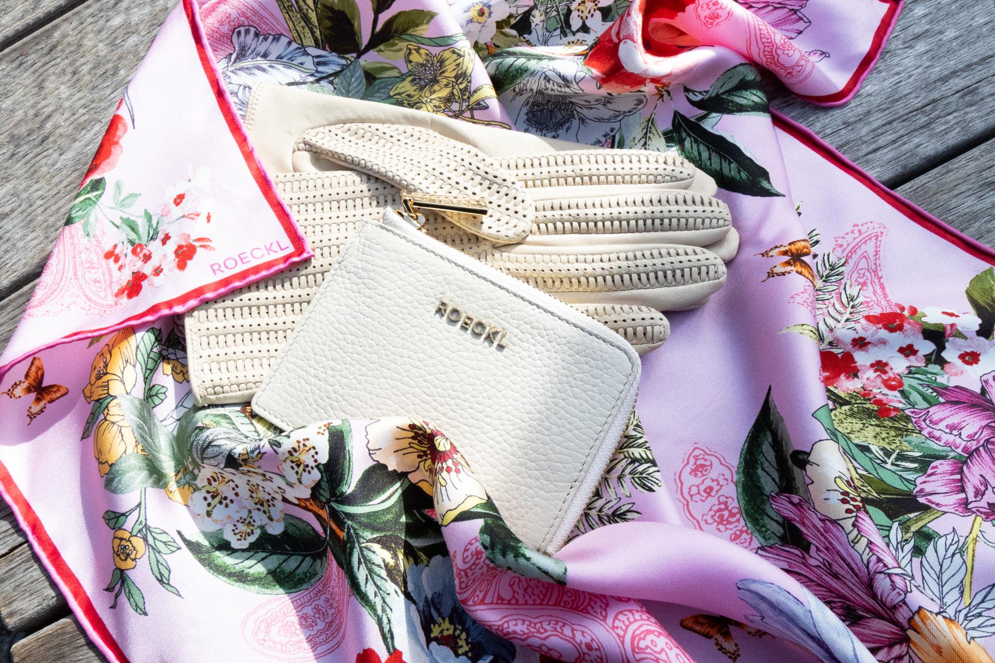 Beigefarbene ROECKL-Lederhandschuhe und Lederportemonnaie auf floralem Seidentuch – elegante Accessoire-Kombination mit Liebe zum Detail.