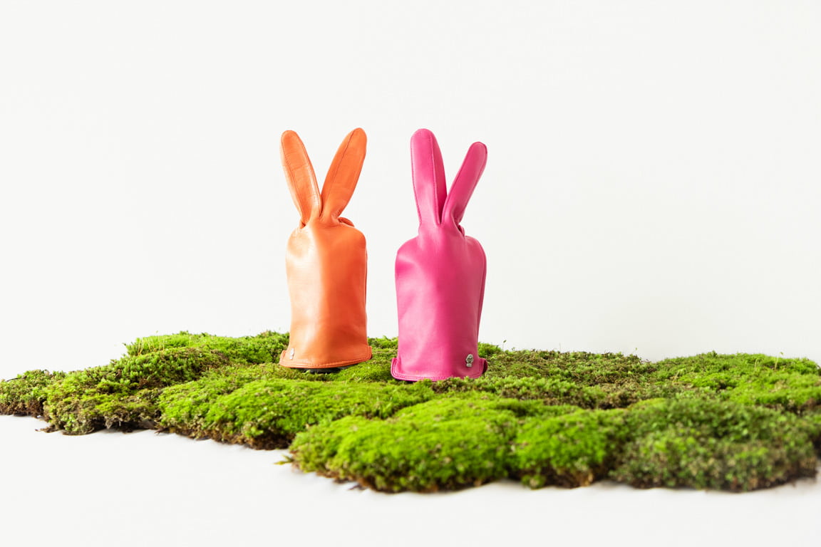 Auf einem grünen Moos stehen zwei Lederhandschuhe, die zu Osterhasen geformt wurden.