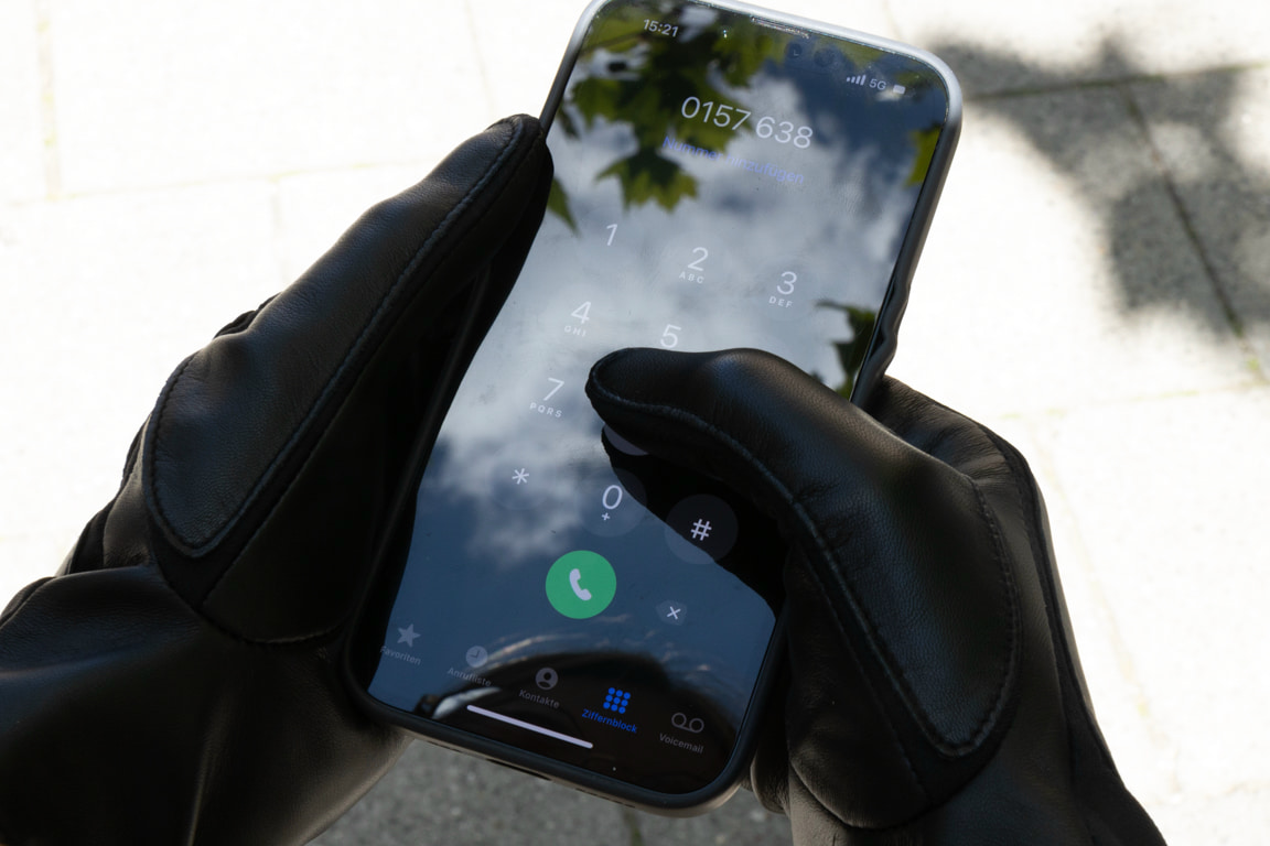 Schwarze ROECKL-Lederhandschuhe mit Touchscreen-Funktion beim Wählen auf dem Smartphone – elegantes Accessoire mit moderner Technologie.