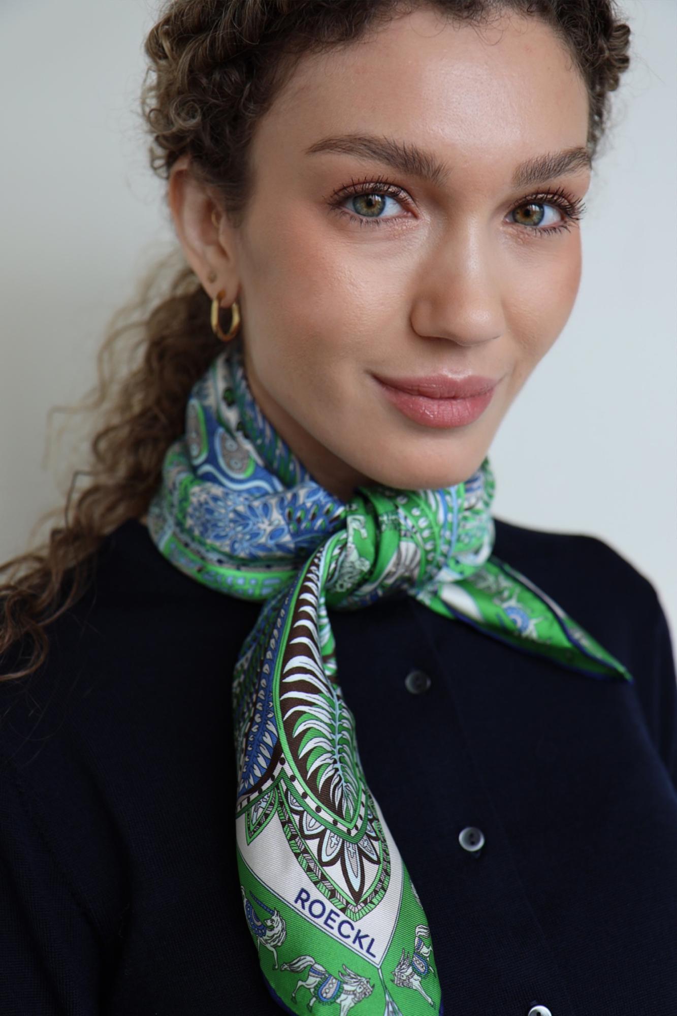 Frau mit cremefarbenem ROECKL-Seidentuch mit floralem Muster – elegantes Kopftuch als edles Mode-Statement zu beigefarbenem Mantel.