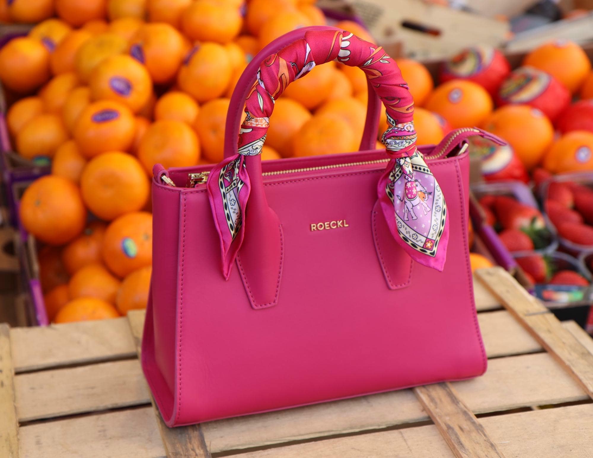 A pink velvet scarf tied around the handle of a pink leather bag named Ruby.