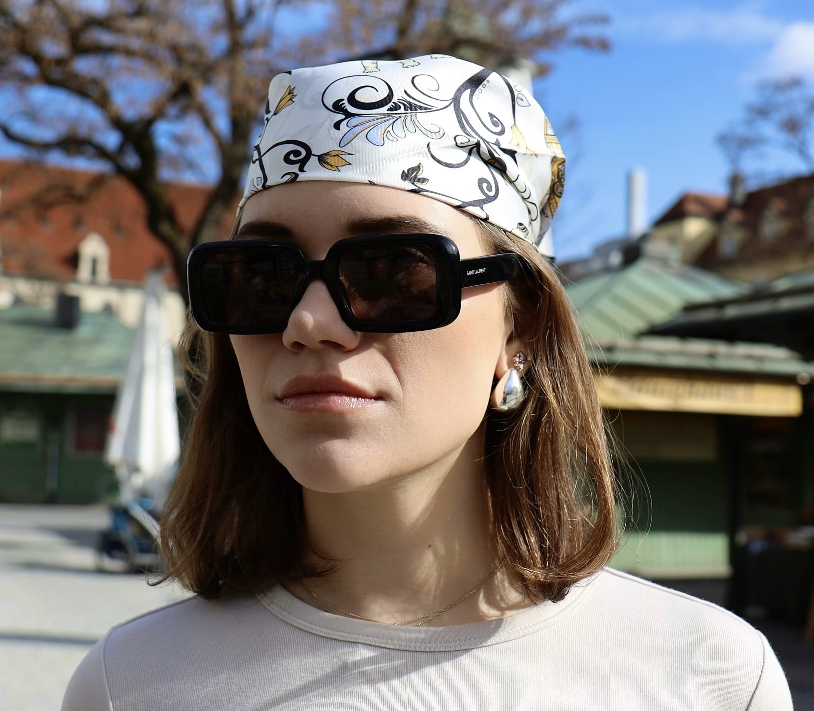 A beige silk neck scarf that is tied around the head as a headscarf.