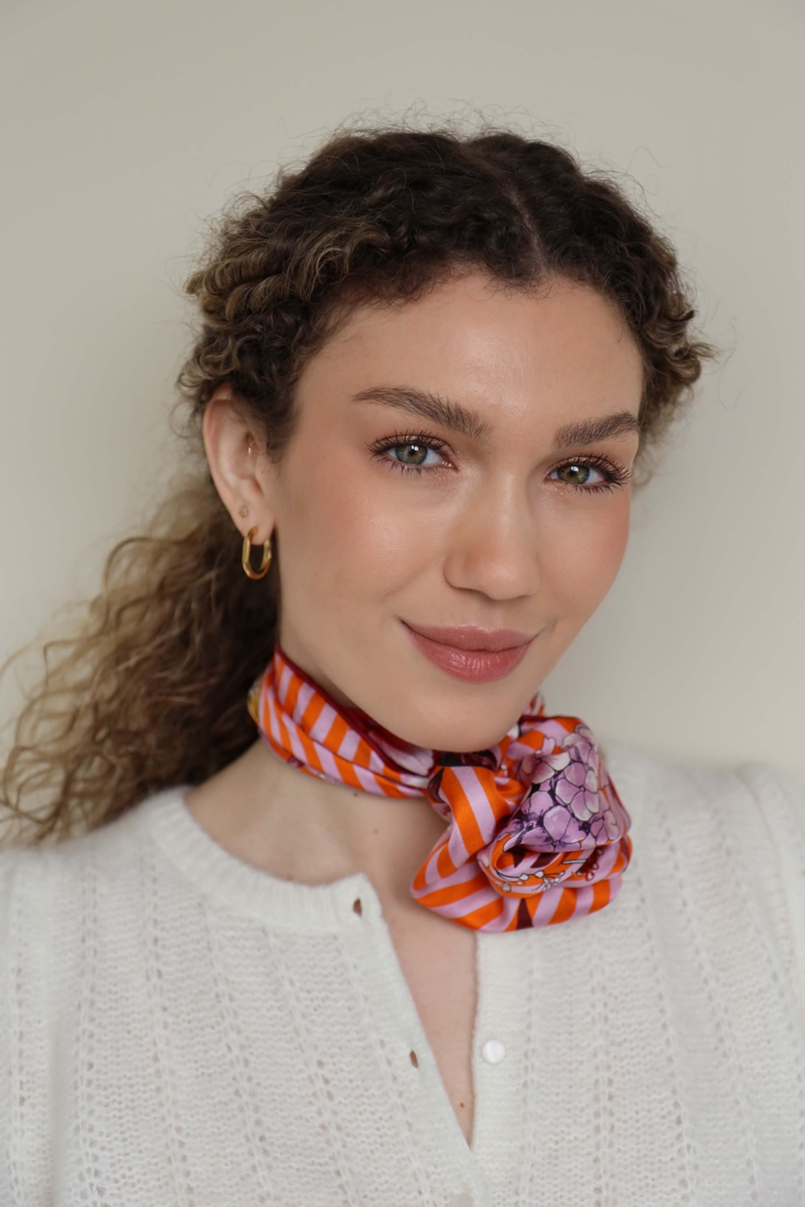 Modern gebundenes Halstuch für Damen im Rosettenknoten – kleines Seidentuch mit orange-rosa Streifen und floralen Blumenmustern, elegant am Hals getragen